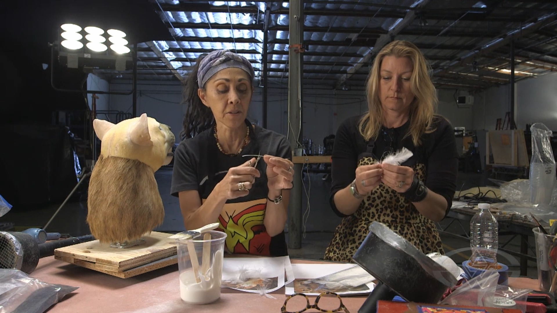 Deborah Galvez cuts her whisker so all the whiskers differ in length, while Connie Criswell strips a feather.