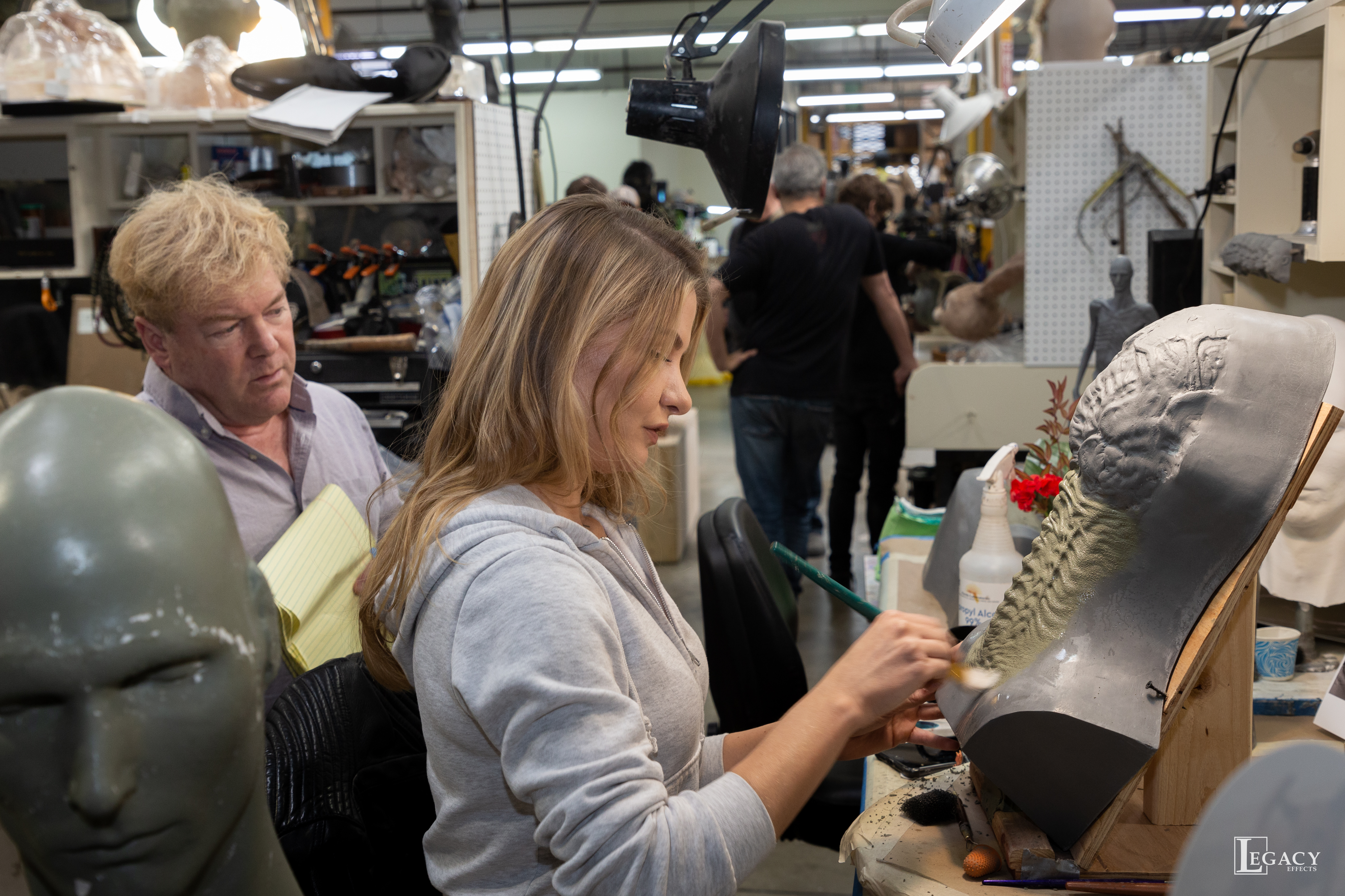 Shane Mahan reviews Savannah Suderman's sculpting progress on the Offspring's neck appliance. Image courtesy Legacy Effects.